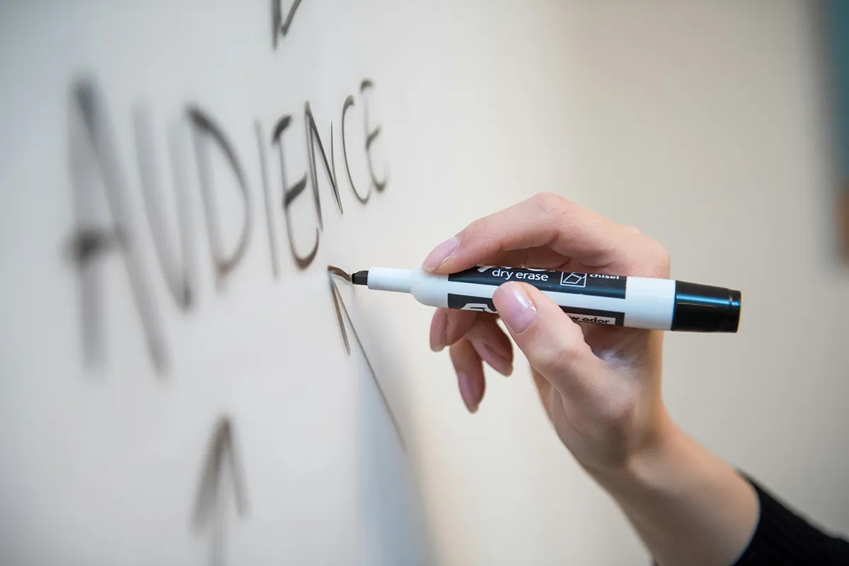 A woman is writing the word Audience and drawing arrows on a whiteboard.