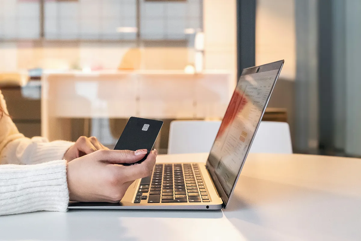 A woman is holding a credit card in front of her laptop.