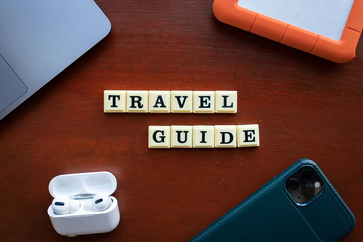 The words Travel Guide written with Scrabble letters on a wooden surface.